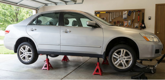 Silver car safely supported by four red jack stands in a clean garage.