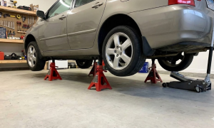 Beige car elevated safely on four red jack stands in a home garage.