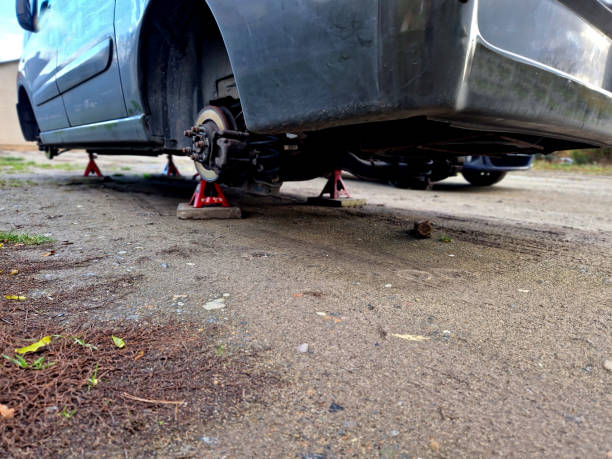 Car raised on red jack stands on dirt, wheels removed for maintenance.