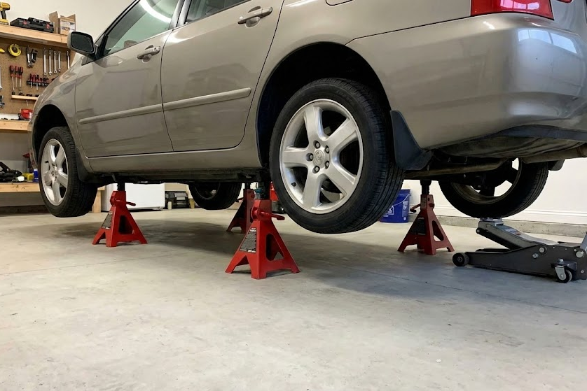 Car safely elevated on four red Jack Stands in a garage for maintenance.