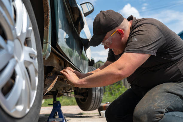 Man using jack stands to safely work on a rusty car's underside.