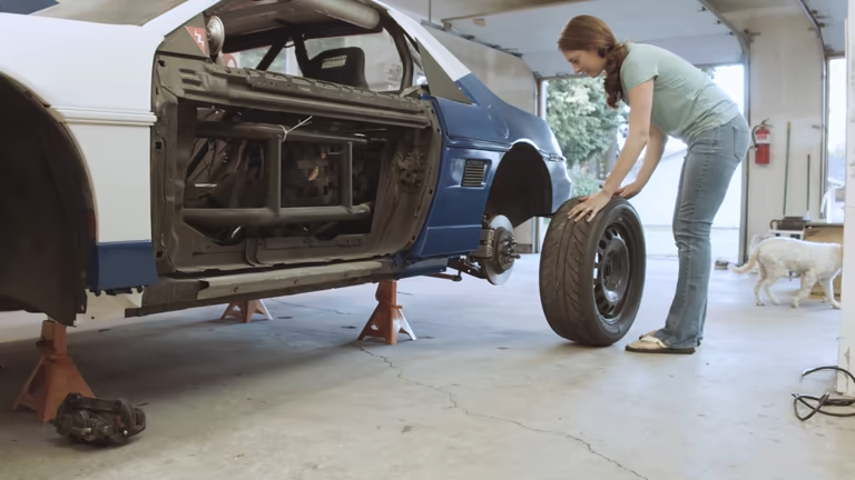 Woman replacing car tire. Car lifted securely using orange Jack Stands.