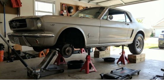 Classic Mustang lifted in a garage, safely supported by multiple jack stands and wood blocks.