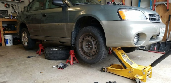 Car lifted for tire change in garage, secured by sturdy red jack stands.