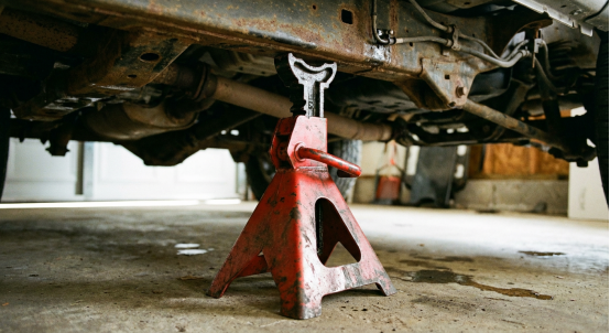 A robust red Jack Stand securely supports a rusty vehicle frame during repair work.