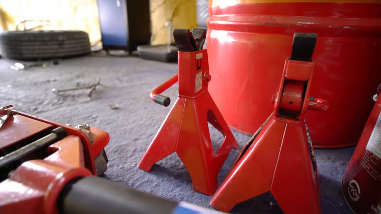 Two red jack stands on a garage floor with a floor jack nearby.