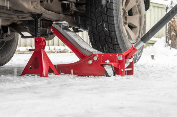 Red hydraulic jack and jack stands lifting a car on a snowy driveway.