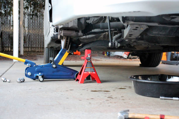 Car lifted with a jack, secured by a red jack stand for maintenance.