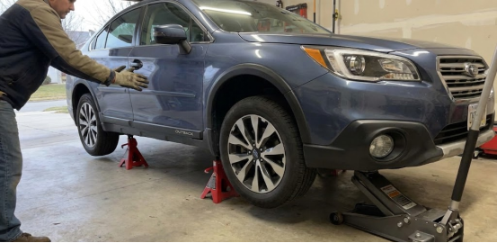 Man checking blue car supported by jack stands and a floor jack in a garage.