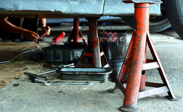 Person working under car safely supported by two orange jack stands.
