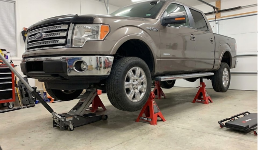 Ford F-150 truck lifted with a floor jack and red jack stands in a garage.