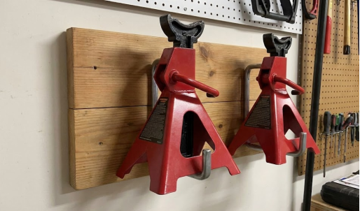 Two red jack stands neatly hung on a wooden wall mount in a garage.