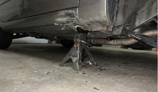 A single jack stand supports a car's undercarriage on a concrete floor.