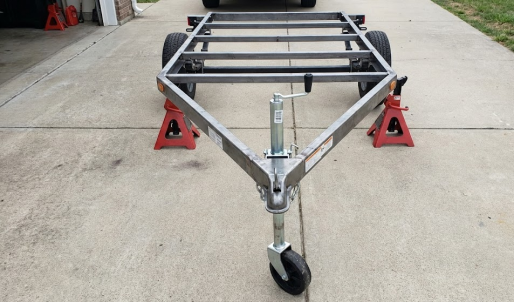 Empty trailer frame safely supported by two red jack stands on a concrete driveway.