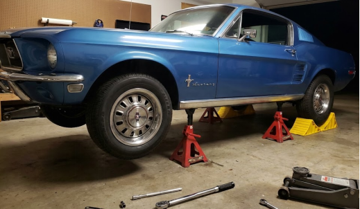 Classic blue Ford Mustang securely raised on red jack stands for maintenance in a garage.