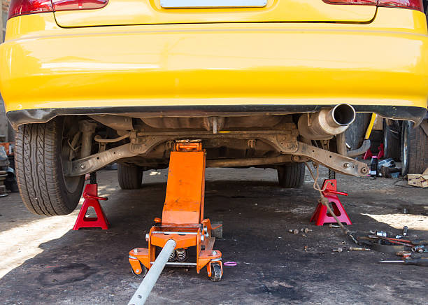 Yellow car lifted by floor jack, safely supported by red jack stands for repair.
