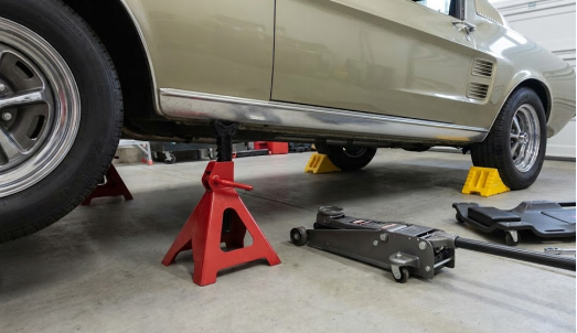 Classic car elevated on a red jack stand, floor jack, and wheel chocks.