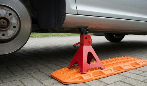 Close-up of a red Jack Stand firmly placed on an orange traction board supporting car.